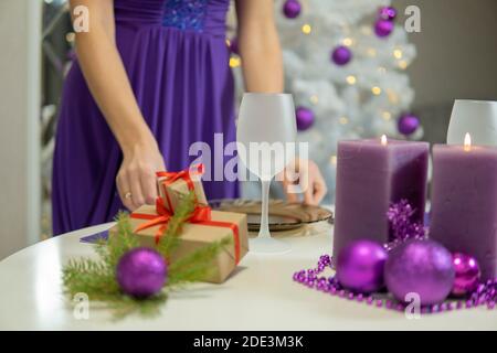 Mädchen macht Weihnachten Tischdekoration mit Geschenken und lila Kerzen.. Hohe Qualität Stockfoto