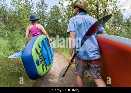 Ein junges Paar trägt Standup-Paddleboards zum Wasser in Oregon. Stockfoto