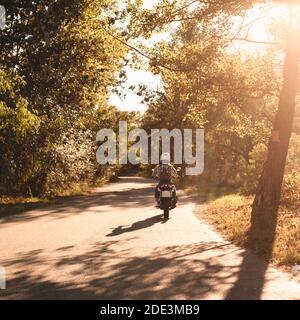 Rückansicht der Frau, die Motorrad auf Landstraße fährt Wald Stockfoto