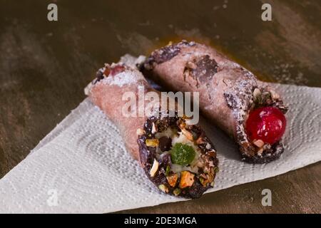Zwei Cannoli, ein italienisches Dessert aus Frischkäse mit Pistazien und Schokolade. Auf einem gelben Tisch. Stockfoto