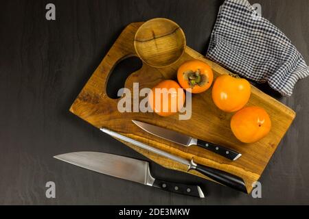 Reife frische Kaki auf rustikalem Hintergrund. Kaki Obst auf Holz Küchentisch. Schneiden von Obst auf einem Küchenbrett. Stockfoto