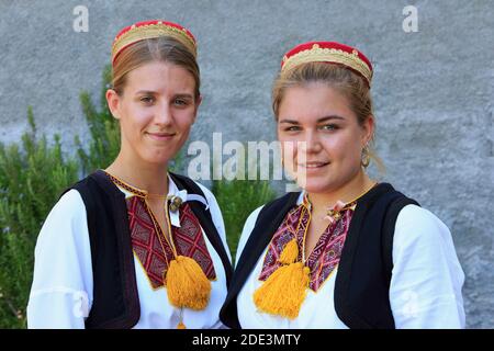 Zwei Mädchen mit einem traditionellen kroatischen roten Filzhut, einem weißen Hemd und einer schwarzen, gestickten Weste in Cilipi, Kroatien Stockfoto