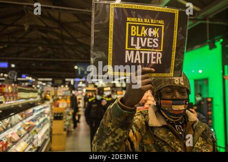 Ein Protestant mit einem Plakat, auf dem steht: "Black Lives Matter" während der Demonstration der Tod des 40-jährigen João Alberto Silveira, eines schwarzen Mannes, der am 19. November in Porto Alegre, Brasilien, von Carrefour Vigilanten brutal geschlagen wurde, hat eine Protestwelle in mehreren brasilianischen Städten ausgelöst. In Barcelona machen antirassistische Gruppen vor dem Carrefour auf Las Ramblas einen Akt der Ablehnung. Stockfoto