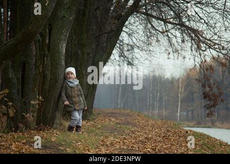 Ein kleines Mädchen steht im Herbst pensiver am Flussufer. Stockfoto