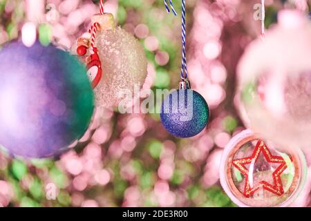 Blaue kugelförmige Dekoration mit winzigen Glitzern und andere schöne bedeckt Dekorative Kugeln hängen vor der Kamera an bunten Weihnachten Hintergrund Stockfoto