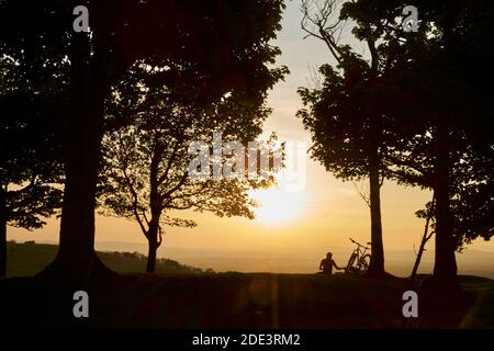 Ein Mann mit Fahrrad sieht einen Sonnenuntergang auf dem Hügel auf dem South Downs Way, England, Großbritannien Stockfoto