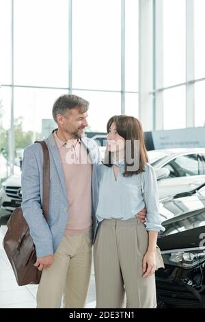 Liebevolles Paar mittleren Alters in smart casualwear Blick auf ein Eine weitere vor der Kamera in großen Auto-Center gegen Verschiedene Autos Stockfoto