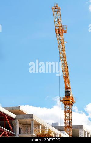 Ein Turmkran-Jib springt über eine Baustelle gegen einen klaren blauen Himmel, vertikales Bild, Kopierraum. Stockfoto