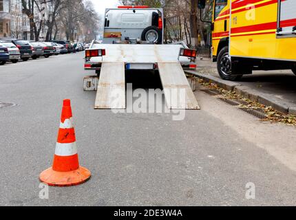 Ein leuchtend oranger Verkehrskegel steht auf dem dunklen Asphalt und zäunt die Fahrbahn mit einem geparkten Transporter. Stockfoto