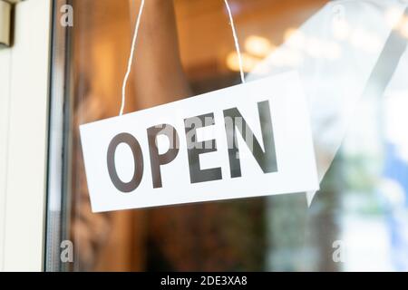 Afrikanischer Kellner hängend Papier mit Hinweis offen an transparente Tür Von modernen Café oder Restaurant vor Beginn der Arbeit in der Morgen Stockfoto