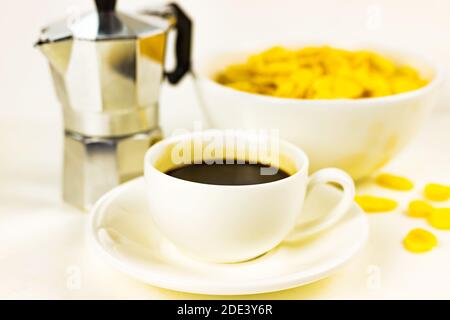 Cornflakes in weißer Schüssel, Tasse Espresso mit schwarzem Kaffee, Geysir-Kaffeemaschine auf weißem Hintergrund Stockfoto