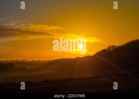 Sonnenuntergang über den Hügeln neben einem Wald in Hertfordshire, malerische orange und rote Sonne mit Wolke in der Dämmerung in einem kalten Herbsttag, malerische Natur Stockfoto