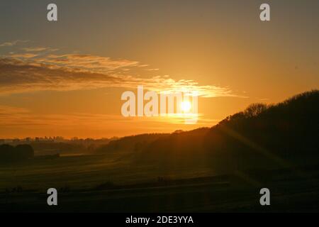 Sonnenuntergang über den Hügeln neben einem Wald in Hertfordshire, malerische orange und rote Sonne mit Wolke in der Dämmerung in einem kalten Herbsttag, malerische Natur Stockfoto