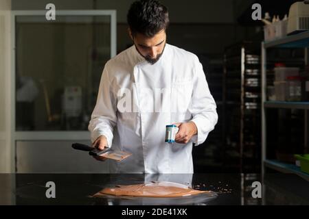 Der Konditor misst die Temperatur der Schokolade mit einem Infrarot-Thermometer und arbeitet an der Temperierung der Schokolade. Stockfoto