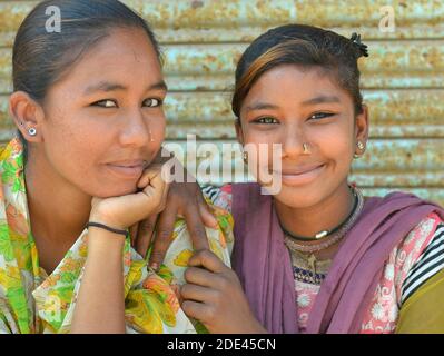 Zwei fröhliche indische Gujarati Mädchen aus Kutch posieren gemeinsam für die Kamera vor einem rostigen Stahl-Shutter-Hintergrund. Stockfoto