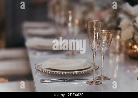 Sektgläser auf dem Tisch. Luxus-Tisch im Restaurant. Gläser und Teller. Dekorationen. Weißer Hintergrund. Hochzeitsbankett. Stockfoto