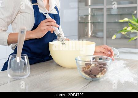 Weibliche Bäcker in blaue Schürze mischen Teig in große Schüssel. Prozess der Herstellung einer Torte oder Muffins Stockfoto