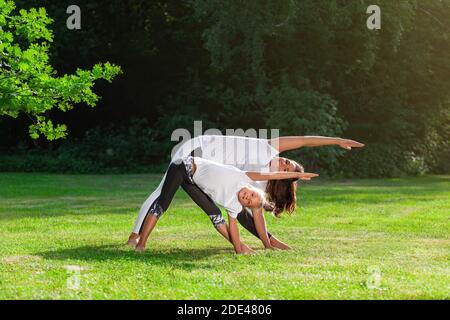 Mutter und kleine Tochter zusammen macht Yoga Asana oder Pilates Training Übung auf grünem Gras im Sommerpark und lächelt. Konzept der Familie outd Stockfoto