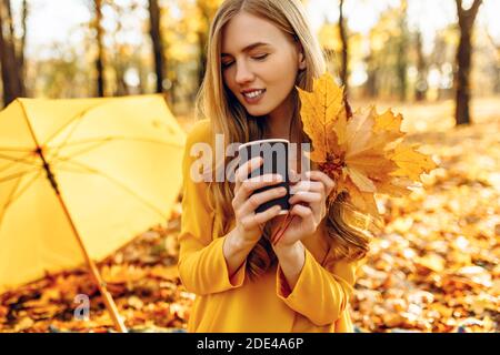 Schöne glückliche junge Mädchen im Herbst Park, mit bunten Herbst Hintergrund, sitzen auf Decke, trinken Heißgetränk, hält Herbstblätter in den Händen, de Stockfoto