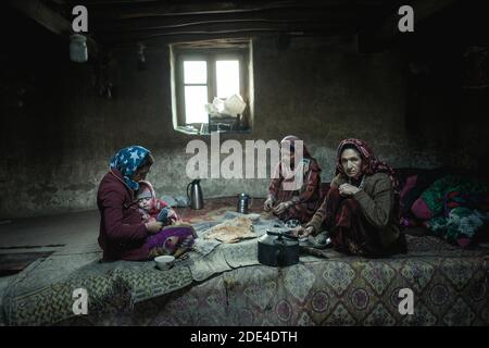 Eine Frau mit einem Kleinkind und zwei weitere Frauen sitzen auf Teppichen im Wohnzimmer eines traditionellen Schlammhauses, Khandud, Wachan Korridor, Afghanistan Stockfoto