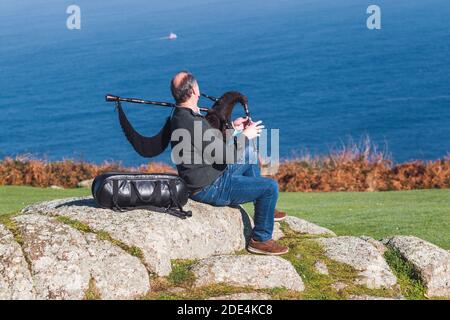 Blick von hinten auf Dudelsackläufer, der auf einem Felsen sitzt und spielt Die Dudelsäcke mit dem Turm von Hecules im Hintergrund Im Nebel Stockfoto