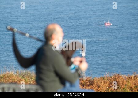 Blick von hinten auf Dudelsackläufer, der auf einem Felsen sitzt und spielt Die Dudelsäcke mit dem Turm von Hecules im Hintergrund Im Nebel Stockfoto