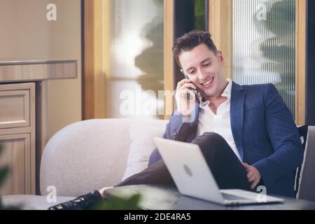 Der junge, gutaussehende Geschäftsmann lächelt am Telefon und sitzt am Tisch im Café Stockfoto