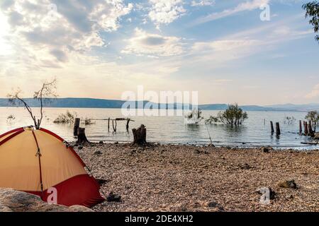 Blick auf den Galiläischen See vor dem Hintergrund der Golanhöhen in Israel. Camping am Ufer des Sees von Galiläa. Rotes Zelt. Wolkiger Blauer Himmel. Hochwertige Fotos Stockfoto