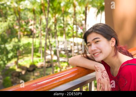 Biracial teen weiblich lächelnd, wie sie lehnt sich auf Geländer Blick Palmen und Kokospalmen an sonnigen Tagen in Hawaii Stockfoto
