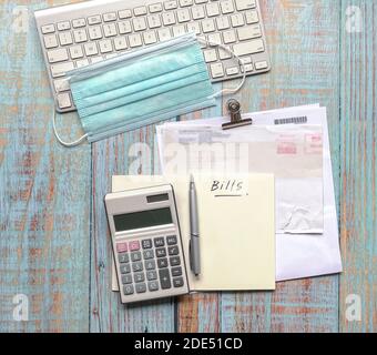 Rechnungen und Taschenrechner, und Tastatur mit Gesichtsmaske auf Holztisch. Draufsicht. Stockfoto