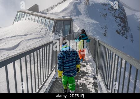 Rückansicht von zwei Kindern, die auf der Brücke auf der Spitze des Berges gehen. Urlaub mit Kindern nach Alps im Winter. Glacier 3000, Les Diablerets Stockfoto