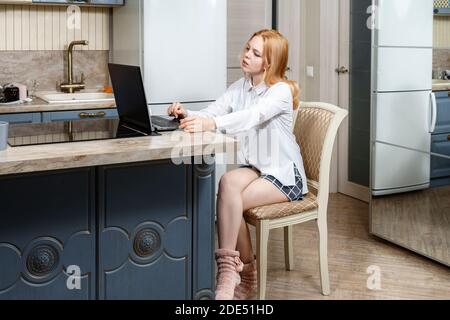 16 Jahre alt schönes rothaariges Mädchen in einer weißen Bluse und hausgemachten Stricksocken kommuniziert mit einem Laptop online. Stockfoto