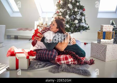 kaukasisches Paar, das im Schlafanzug auf dem Boden sitzt, umarmt, Weihnachtsgeschenke austauscht Stockfoto