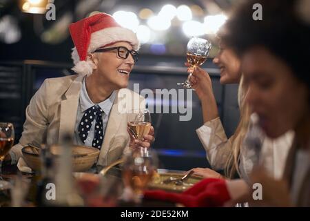 kaukasischen Chef Dame trägt weihnachtsmann Hut mit Brille mit einem Gute Zeit beim Business Dinner am Ende des Erfolgserfolgreichen Jahr mit Kollegen Stockfoto