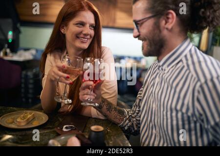 Junge kaukasische tätowierte Mann mit einem Bart Wein trinken mit einem schönen Rothaarige Frau bei einem romantischen Abendessen im Restaurant, toasten, einander suchen Stockfoto