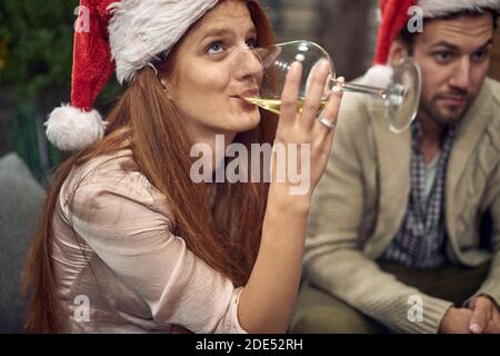 Junge curasische Frau trinkt Weißwein mit weihnachtsmütze und schaut nach oben Stockfoto