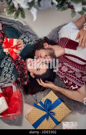 Draufsicht auf glückliche junge, schöne, kaukasische Paar auf dem Boden zu Weihnachten lachend, genießen, mit eingewickelten Geschenken um sie. Weiblich l Stockfoto