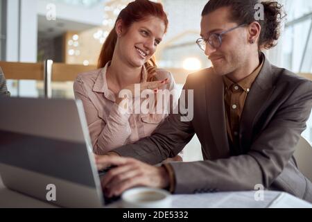 Junge Kollegen bei einer Pause beim Anschauen von Laptop-Inhalten und beim Plaudern in angenehmer Atmosphäre in der Firmenkantine. Menschen, Arbeit, Unternehmen, Geschäftskonzept. Stockfoto