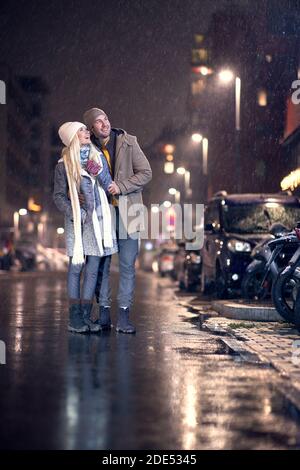 Junges kaukasisches Paar, das aufschaut, lächelt und Schnee fällt sieht Stockfoto