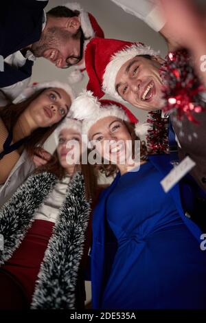 Ansicht von Kollegen im Kreis stehen, Spaß haben, feiern das Ende eines erfolgreichen Jahres, tragen santa Hüte. Christmasime Stockfoto