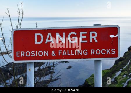 Rote und weiße Zeichen Gefahr Erosion und Falling Rocks an der Klippe Kante in St Andrews, Schottland genommen. Meer und Felsen im Hintergrund unten. Stockfoto