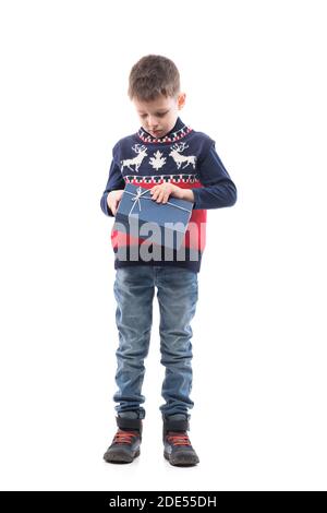 Kleines Kind in Weihnachten Pullover Blick nach unten und Eröffnung Geschenkbox mit leeren reservierten Ausdruck. Ganzkörper-Porträt isoliert auf weißem Hintergrund. Stockfoto