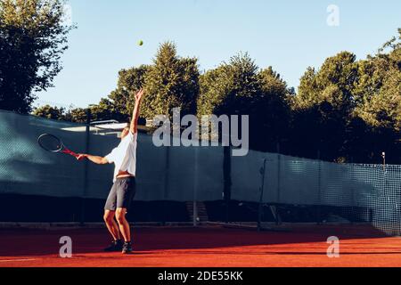 Junger professioneller Tennisspieler, der einen Service leistet Stockfoto
