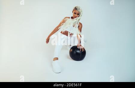 Fit Frau mit langen geflochtenen Haaren, die mit einem Medizinball Fitness-Workout macht. Fitness-Frau, die mit Medizinball auf weißem Hintergrund trainiert. Stockfoto