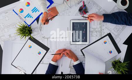 Draufsicht der Architekten, die über Baupläne mit Blaupause sprechen, Analyse der Jahresfinanzberichte. Geschäftsleute Designer diskutieren im Büro mit digitalen Gadgets und Papiere arbeiten. Stockfoto