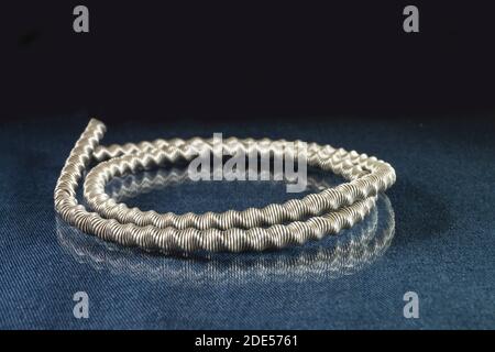 Die metallische Spirale vom Draht auf dem Tisch mit Reflexion. Stahlfeder auf schwarzem Hintergrund Nahaufnahme Stockfoto