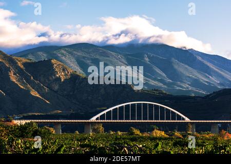 Viadukt der A7, wie es durch Granada über ein Feld von Obstbäumen mit Bergen mit Wolken auf der Spitze passiert. Stockfoto