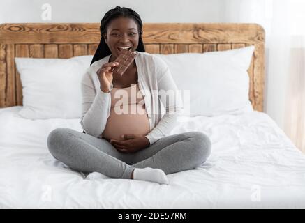 Heißhunger Während Der Schwangerschaft. Fröhliche Zukunft Mutter Essen Schokolade Bar Im Bett Stockfoto