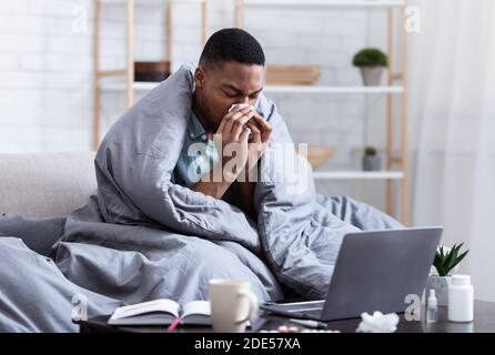 Ill African Man Niesen Und Blasen Nase Sitzen Zu Hause Stockfoto
