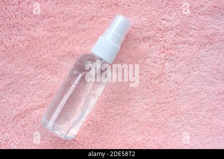 Handdesinfektionsflasche auf weichem rosa Handtuch texturierten Hintergrund. Flache, minimalistische Lay-Komposition. Kovidschutz. Draufsicht, Kopierbereich Stockfoto